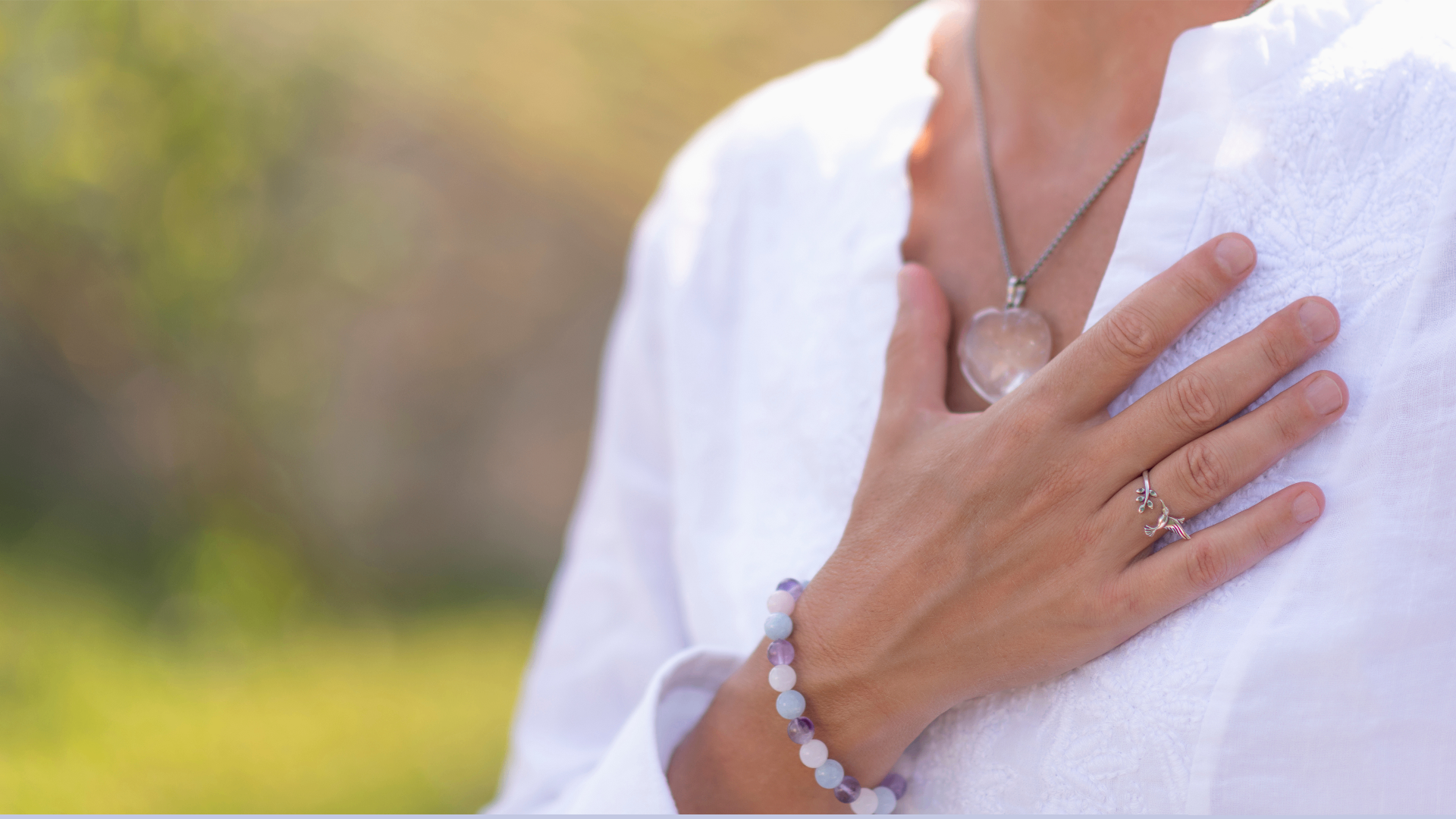 A hand resting gently on the chest with a rose quartz heart pendant, in soft golden light
