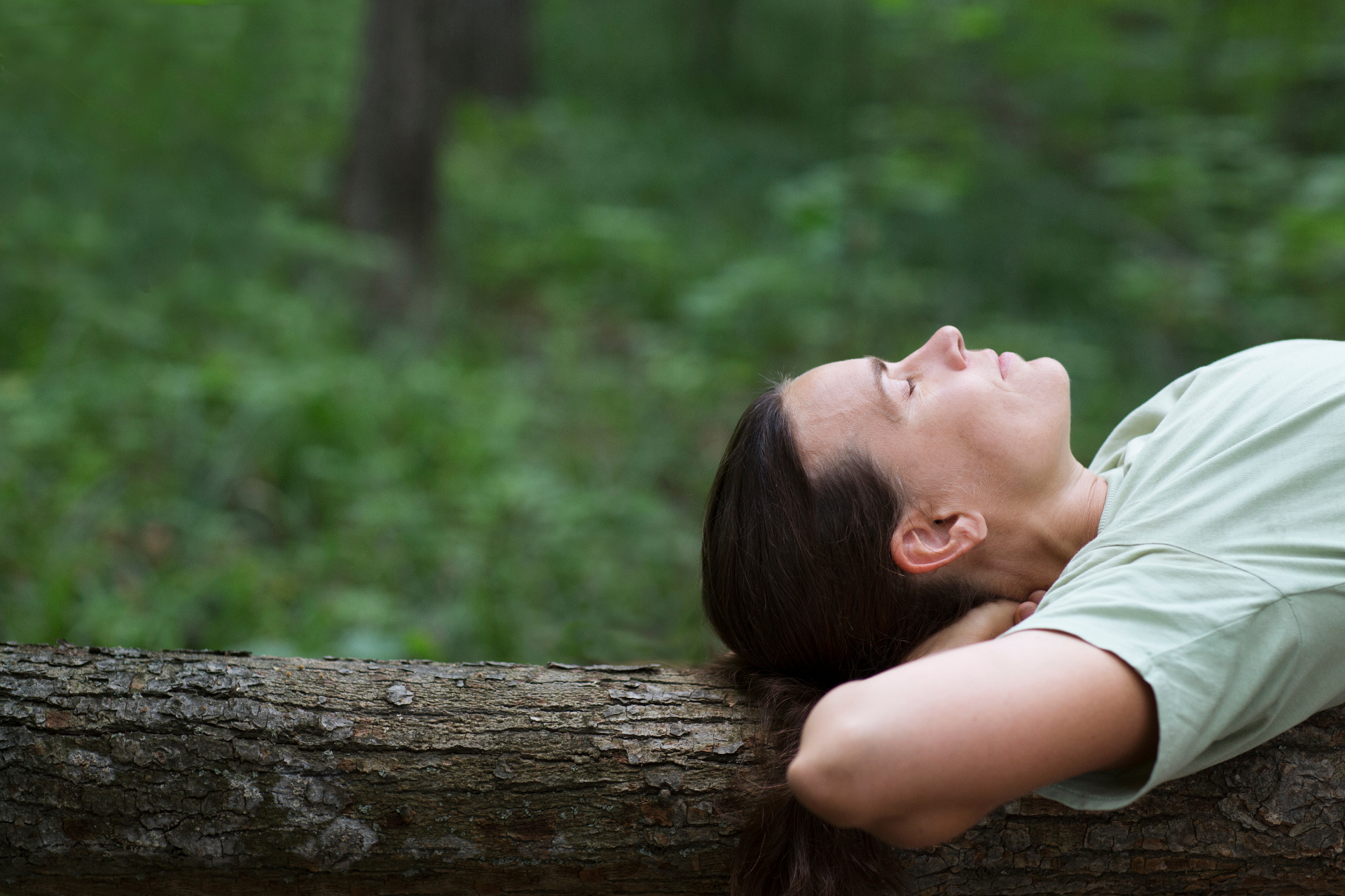 Woman resting peacefully on a log in a green forest